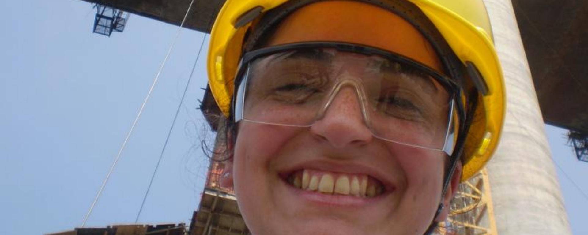 La graduada en una obra. Ingeniera mira a cámara con casco y lentes de protección.