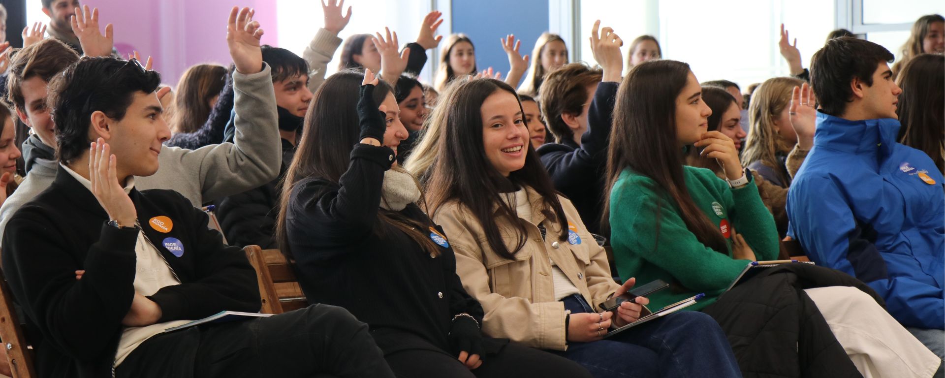 Preuniversitarios sentados en filas, participando de la Experiencia UM, levantan la mano.